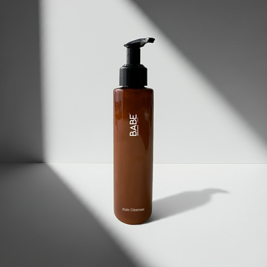 Brown pump bottle of Babe Kale Face Cleanser on white surface with shadow background