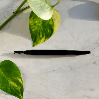 Automatic eyebrow pencil with dual-tip design on a marble surface, surrounded by green leaves.