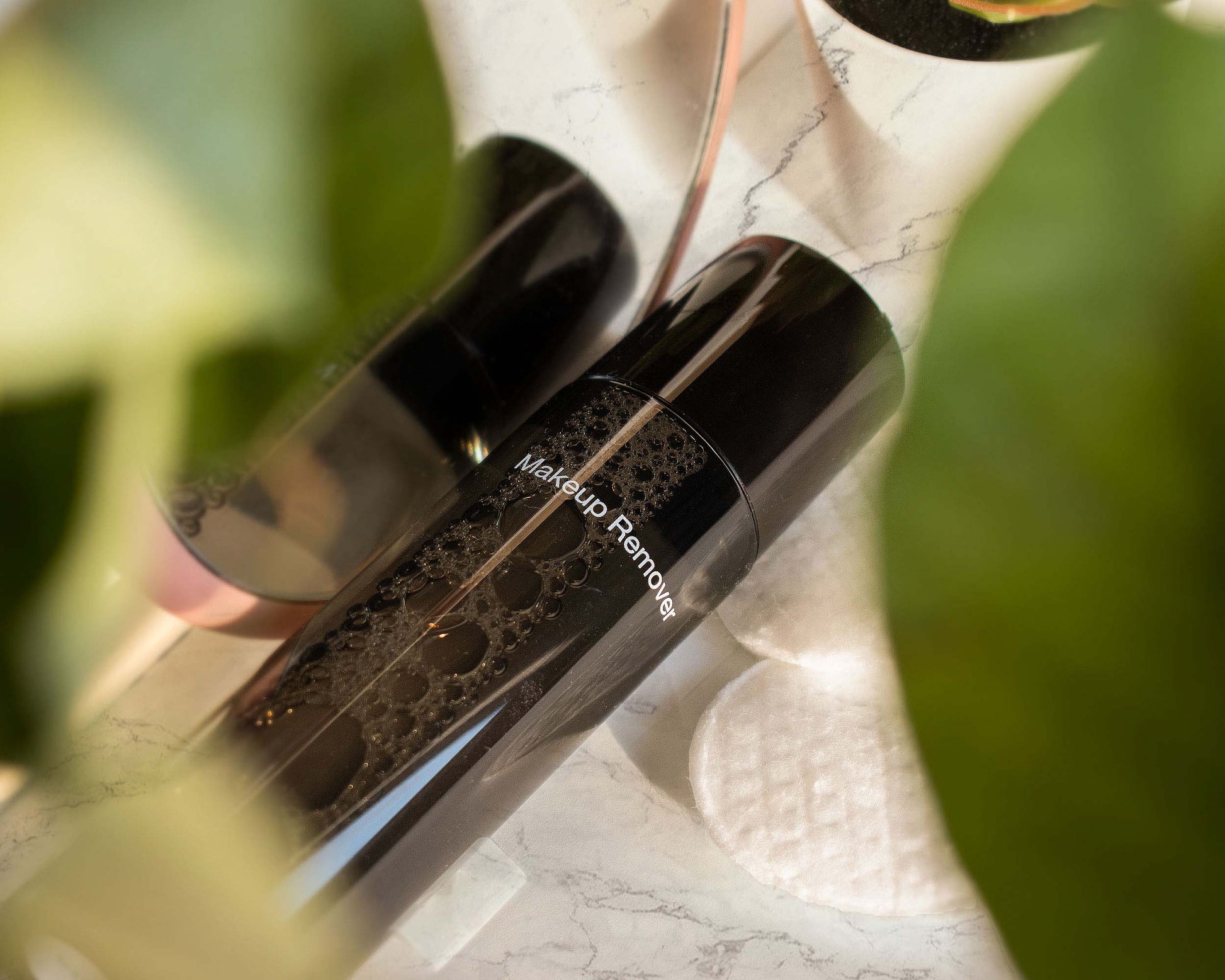 Makeup Remover Solution bottle on marble surface with cotton pads nearby.