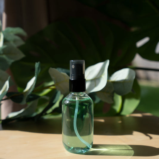 Lightweight setting spray in a clear bottle on a wooden table with plant leaves in the background.