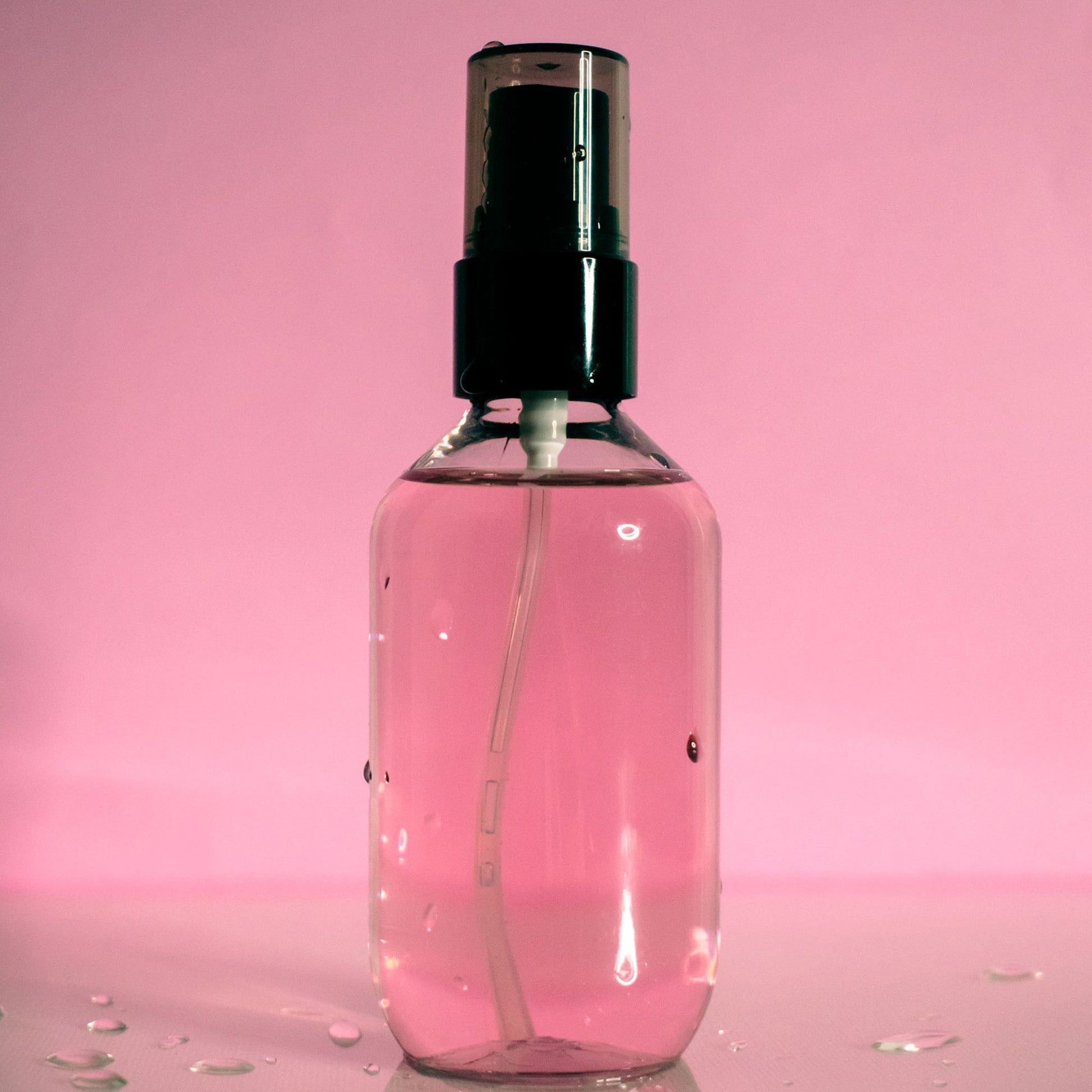 Oil Control Setting Spray in transparent bottle with black cap on pink background.